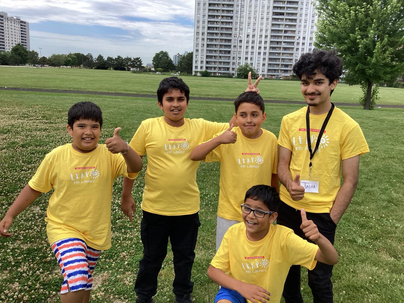 Photo of four LiftED LEAP into Literacy Summer Day Camp program participants and one volunteer standing in a park and smiling at the camera