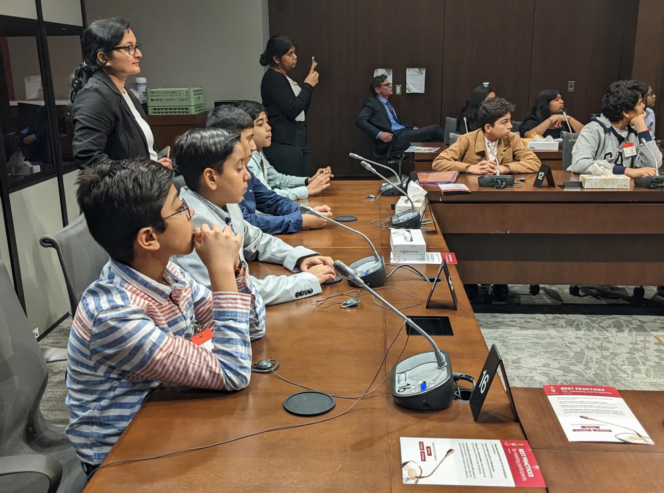 Photo of LiftED Take the LEAD program participants sitting around a large debate table equipped with microphones